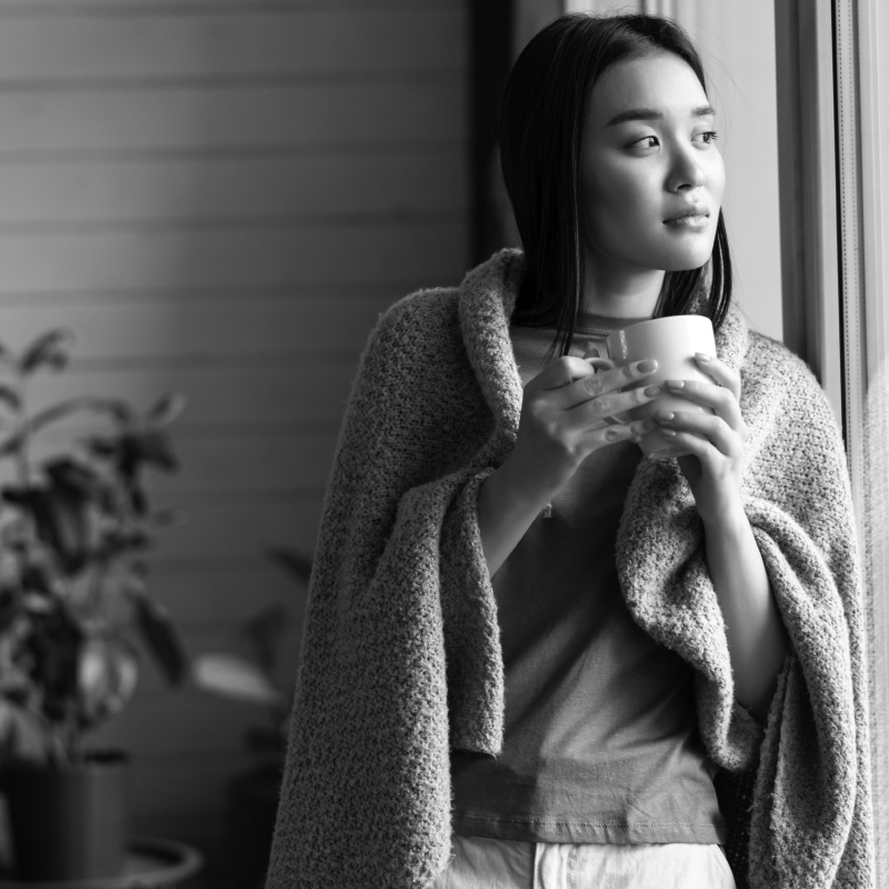 B&W image of an asian woman drinking tea and looking out the window